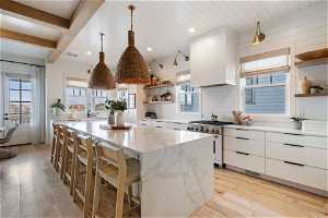 Kitchen with white cabinets, a kitchen island, light wood-type flooring, and high end stove
