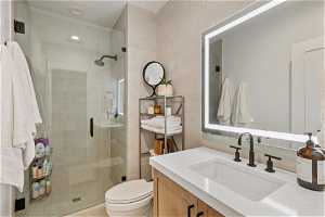 Bathroom with walk in shower, toilet, vanity with extensive cabinet space, and tile walls