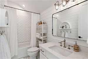 Full bathroom featuring wooden walls, toilet, vanity, and shower / tub combo with curtain