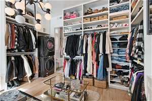 Spacious closet with stacked washer / dryer, a notable chandelier, and light hardwood / wood-style flooring