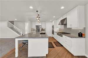 Kitchen with light colored carpet, an island with sink, appliances with stainless steel finishes, decorative light fixtures, and a breakfast bar
