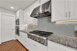 Kitchen featuring white cabinets, tasteful backsplash, light stone countertops, and light wood-type flooring