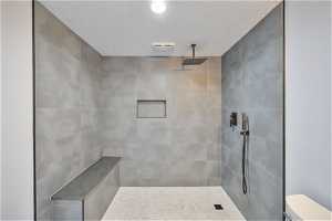 Bathroom featuring a textured ceiling, toilet, and tiled shower