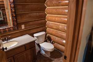 Bathroom with tile flooring, oversized vanity, log walls, and toilet