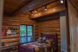 Bedroom with beam ceiling, log walls, rail lighting, and wood ceiling