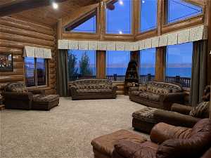 Carpeted living room featuring high vaulted ceiling, log walls, wooden ceiling, and a water view