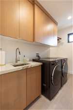 Clothes washing area with sink, washer and dryer, washer hookup, light tile floors, and cabinets