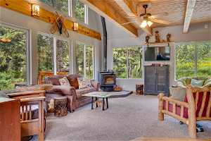 Sunroom / solarium with a wood stove, wooden ceiling, ceiling fan, and beamed ceiling