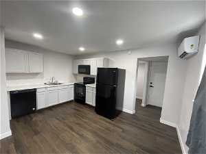 Kitchen featuring black appliances, dark hardwood / wood-style flooring, a wall mounted air conditioner, and white cabinetry