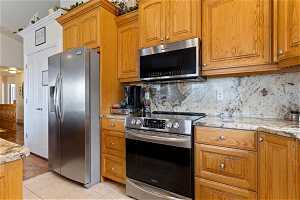 Kitchen with appliances with stainless steel finishes, light tile flooring, light stone countertops, and backsplash