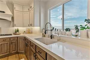 Kitchen with white cabinetry, sink, premium range hood, tasteful backsplash, and light hardwood / wood-style floors