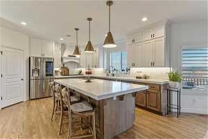 Kitchen with custom range hood, stainless steel fridge, a center island, light hardwood / wood-style floors, and white cabinetry