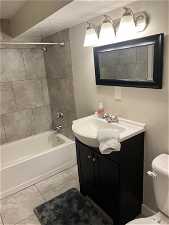 Full bathroom featuring tiled shower / bath combo, tile floors, toilet, and vanity
