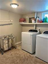 Clothes washing area featuring light colored carpet, a textured ceiling, and washer and dryer