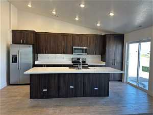 Kitchen featuring vaulted ceiling, a center island with sink, stainless steel appliances, sink, and dark brown cabinets