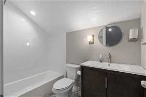 Full bathroom with lofted ceiling, a textured ceiling, tub / shower combination, toilet, and vanity