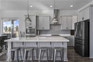Kitchen featuring gray cabinets, wall chimney range hood, hanging light fixtures, dark hardwood / wood-style flooring, and stainless steel appliances