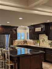 Kitchen featuring sink, dark brown cabinetry, ornamental molding, stainless steel refrigerator with ice dispenser, and dark stone counters