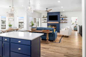 Kitchen with light LVP floors, decorative light fixtures, a large fireplace, a kitchen island, and ceiling fan