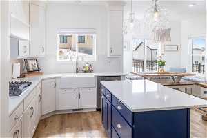Kitchen with white cabinetry, light LVP flooring, blue cabinetry, and hanging light fixtures