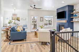 Living room with light LVP flooring, ceiling fan with notable chandelier, and a large fireplace