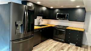 Kitchen with sink, tasteful backsplash, butcher block counters, light hardwood / wood-style floors, and black appliances