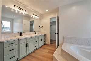 Bathroom with dual vanity, hardwood / wood-style flooring, and tiled bath
