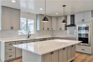 Kitchen featuring appliances with stainless steel finishes, a center island, sink, and wall chimney range hood