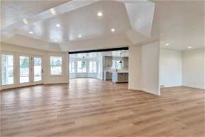 Unfurnished living room featuring french doors, a tray ceiling, a textured ceiling, and light hardwood / wood-style flooring
