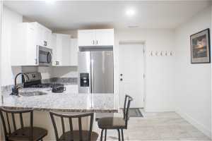 Kitchen with light stone countertops, white cabinets, sink, a breakfast bar, and appliances with stainless steel finishes