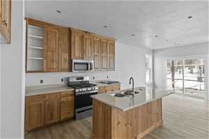 Kitchen featuring appliances with stainless steel finishes, light hardwood / wood-style flooring, sink, and a center island with sink
