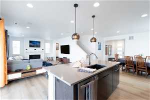 Kitchen with sink, an island with sink, stainless steel dishwasher, decorative light fixtures, and light hardwood / wood-style flooring