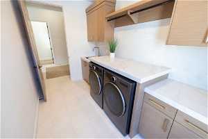 Laundry room with light tile flooring, washing machine and dryer, cabinets, and sink