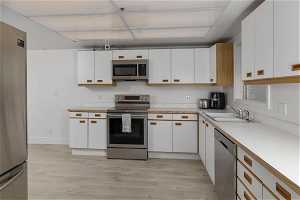 Kitchen with white cabinets, light hardwood / wood-style flooring, stainless steel appliances, and sink