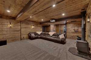 Cinema room with beamed ceiling, wooden walls, a wood stove, wood ceiling, and dark carpet