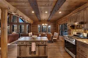 Kitchen featuring dark hardwood / wood-style floors, rustic walls, beam ceiling, an inviting chandelier, and stainless steel range with gas cooktop