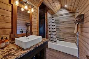 Bathroom with vaulted ceiling, oversized vanity, wood walls, and hardwood / wood-style floors