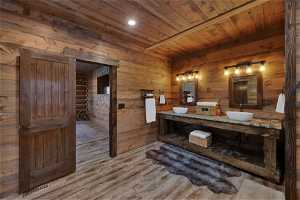 Bathroom featuring dual bowl vanity, wood walls, wooden ceiling, and hardwood / wood-style floors