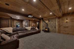 Cinema room featuring wooden walls, beam ceiling, a wood stove, wood ceiling, and carpet floors