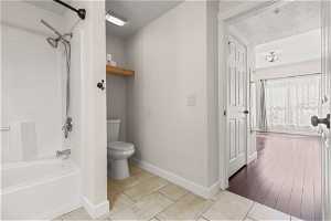Bathroom featuring shower / washtub combination, toilet, tile flooring, and a textured ceiling
