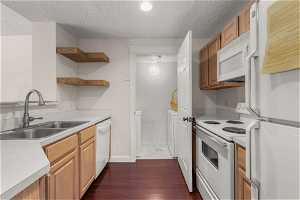 Kitchen with white appliances, dark hardwood / wood-style floors, a textured ceiling, washer / clothes dryer, and sink