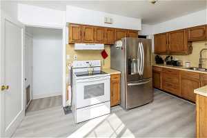 Kitchen featuring light wood-type flooring, stainless steel fridge with ice dispenser, white range with electric stovetop, and sink