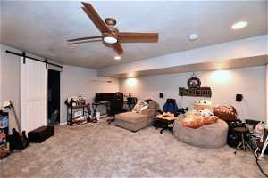 Living room featuring light colored carpet, a barn door, a textured ceiling, and ceiling fan