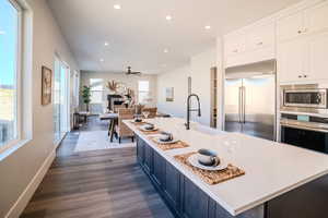 Kitchen with ceiling fan, sink, a kitchen island with sink, built in appliances, and dark hardwood / wood-style flooring