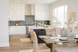 Kitchen with light hardwood / wood-style floors, backsplash, a kitchen island with sink, wall chimney exhaust hood, and white cabinets