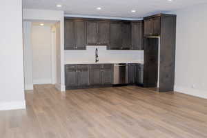 Kitchen with dark brown cabinets, sink, light hardwood / wood-style flooring, and stainless steel dishwasher