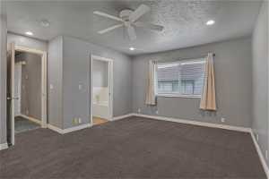 bedroom with ensuite bath, dark carpet, a textured ceiling, and ceiling fan