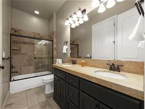 Full bathroom featuring tile flooring, dual bowl vanity, enclosed tub / shower combo, and toilet
