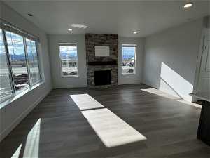Unfurnished living room with a stone fireplace and dark wood-type flooring