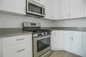 Kitchen featuring appliances with stainless steel finishes, light wood-type flooring, and white cabinets